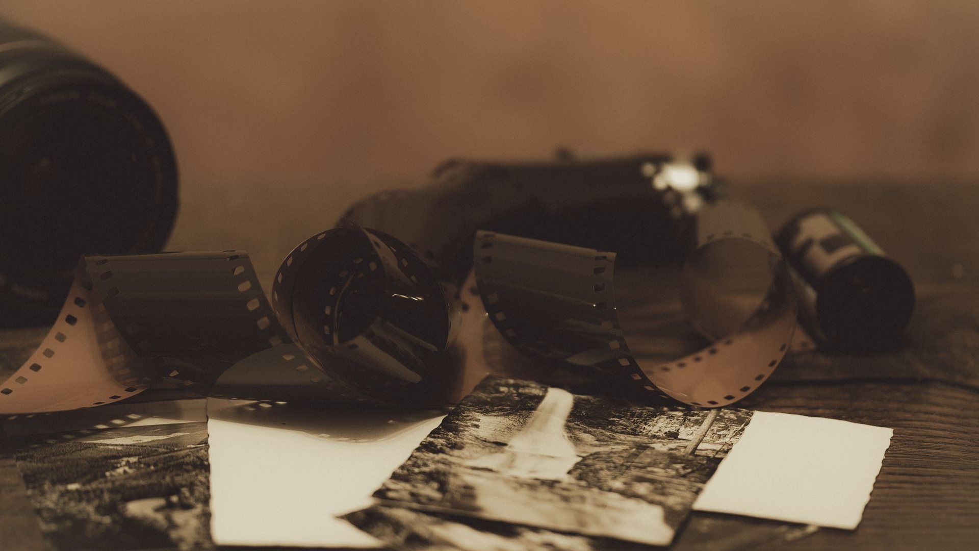 Gulungan film seluloid dan lembaran foto cetak hitam-putih di atas meja kayu