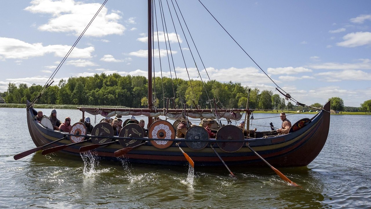 Replika kapal panjang Viking dengan deretan perisai bundar dan awak yang mendayung di danau
