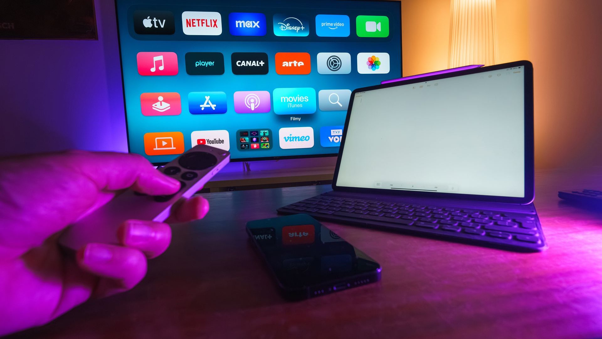 Tangan memegang remote mengarah ke layar televisi yang menampilkan deretan aplikasi streaming
