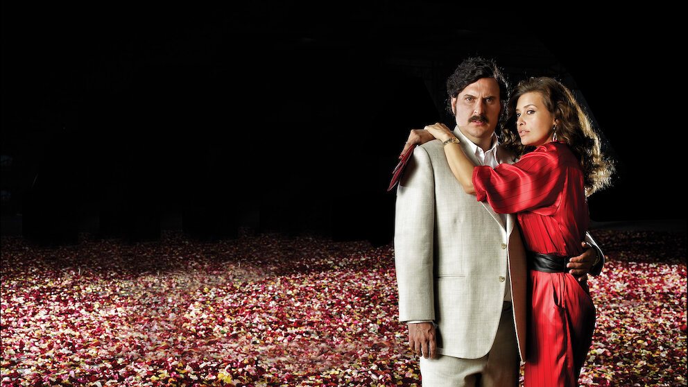 Materi promosi serial Pablo Escobar, el patrón del mal dengan Andrés Parra sebagai Escobar dan seorang perempuan bergaun merah di hamparan kelopak bunga