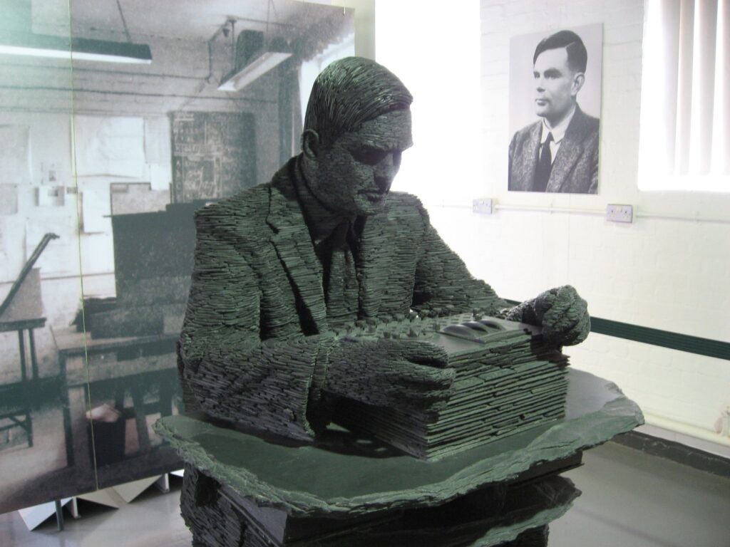 Patung batu sabak Alan Turing karya Stephen Kettle yang duduk menghadap mesin Enigma di Bletchley Park