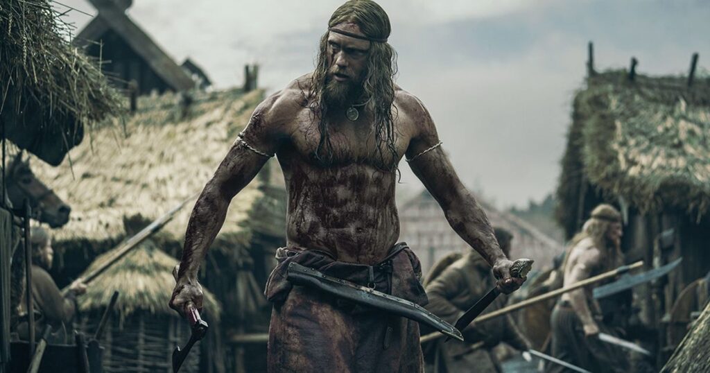 Alexander Skarsgård sebagai Amleth berdiri berlumur darah sambil memegang senjata di desa beratap jerami dalam film The Northman